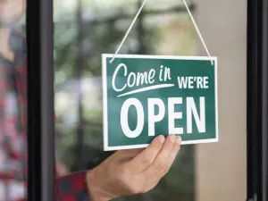 someone on the other side of a widow holding a sign saying "come in we're open"