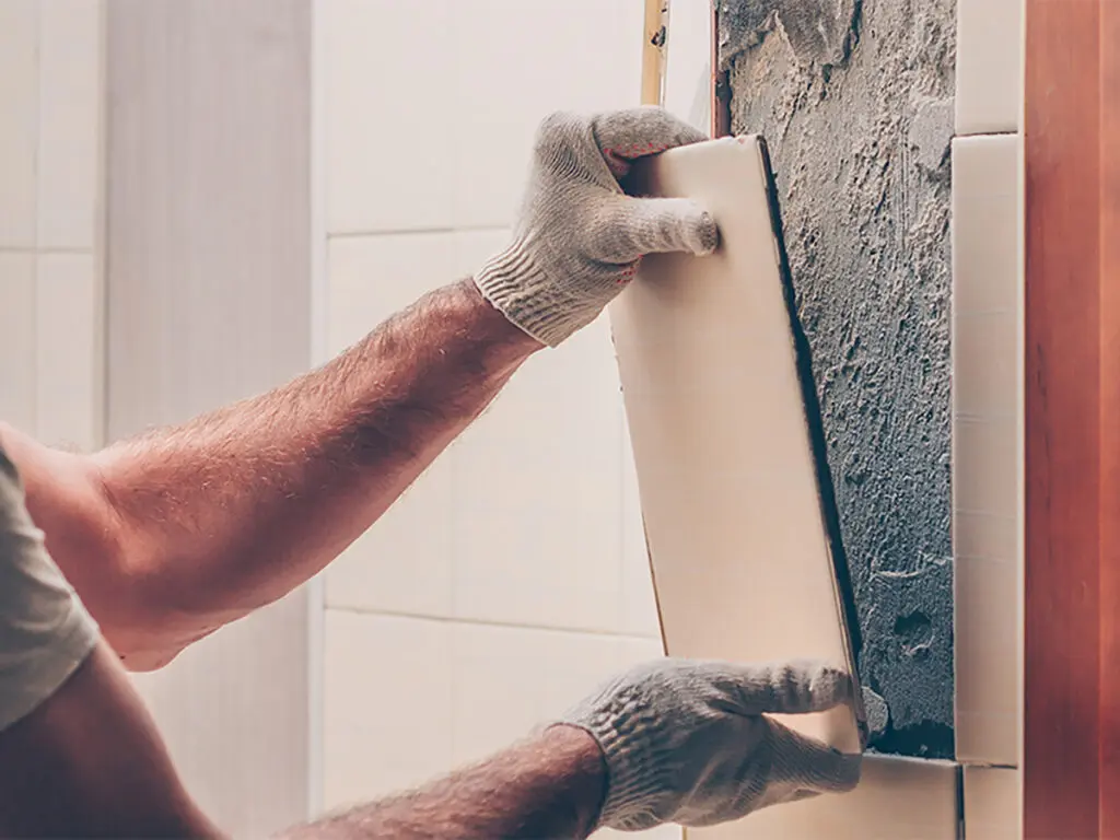 a worker with gloves on putting a piece of tile up on a wall to reconstruct it
